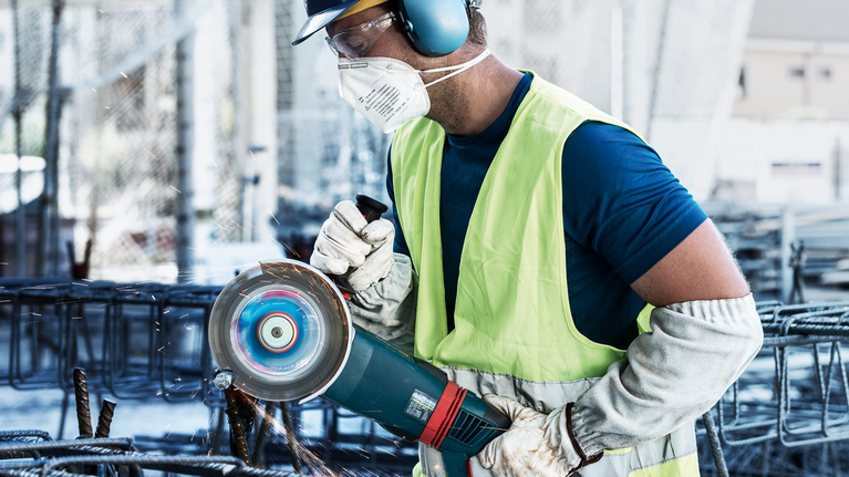 一名配戴安全設備的人用電動工具研磨金屬鋼筋，產生火花。