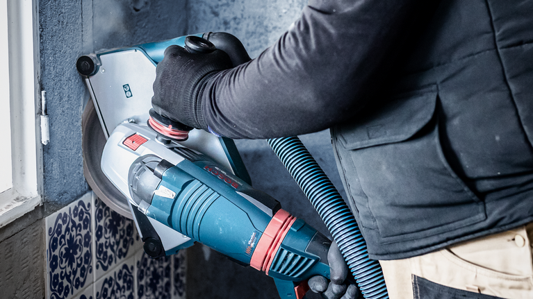 配戴安全設備的人員操作具有除塵功能的牆面研磨機。