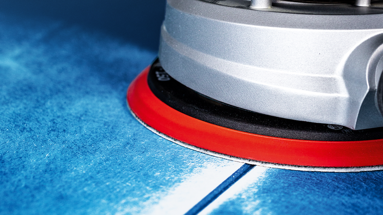 帶有紅色底座的電動工具正在打磨藍色表面。
