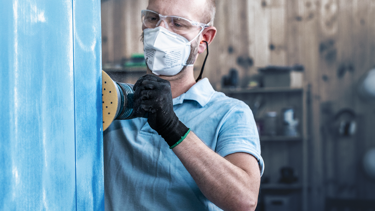 配戴安全設備的人員使用電動砂光機打磨藍色面板。