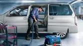一名工人在車庫裡的工具車旁用吸塵器清潔汽車內部。