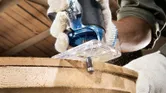 一名佩戴安全設備的人員使用手持銑刀修整木板的邊緣。