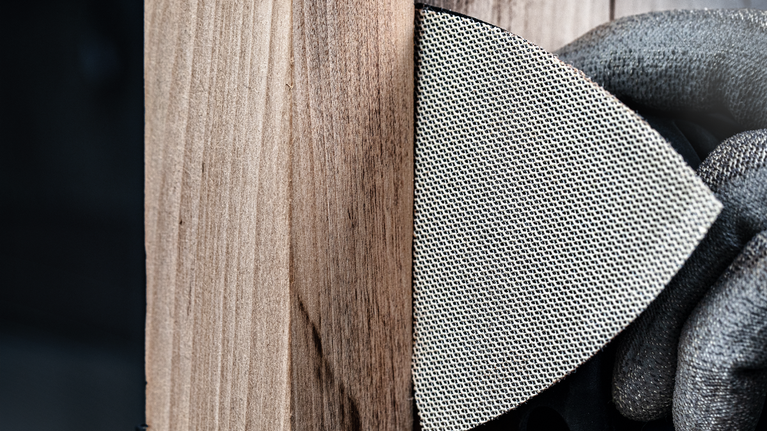 配戴安全設備的人員使用網狀打磨墊打磨木質表面。