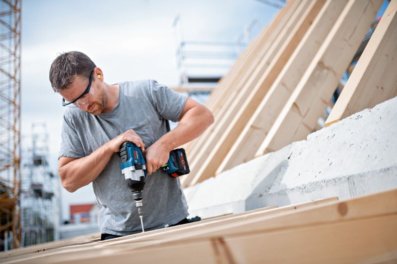 配戴安全設備的人員使用無線衝擊扳手將螺絲轉入木頭。.