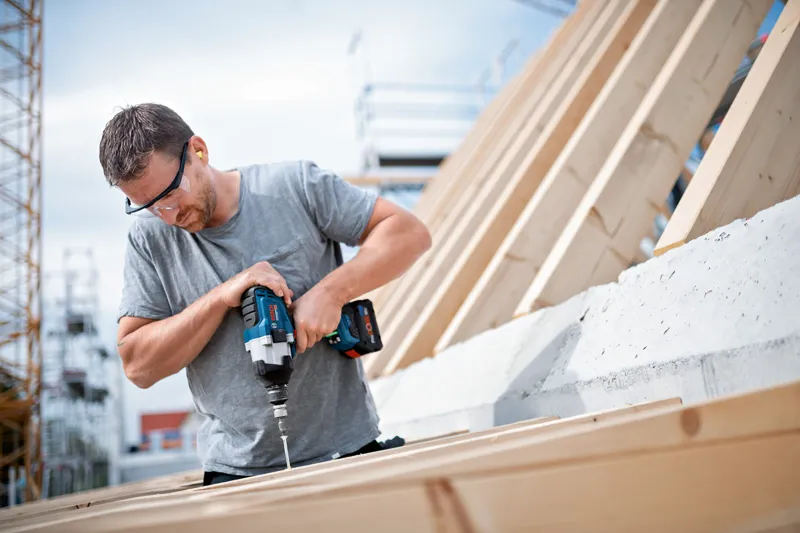 配戴安全設備的人員使用無線衝擊扳手將螺絲轉入木頭。.