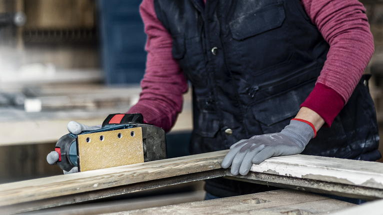 一名配戴安全設備的人員正在用電動砂光機打磨木板。