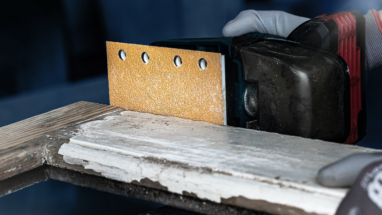 一名配戴安全設備的人員使用無線電動砂光機打磨木材。