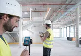 兩名配戴安全設備的人員在正在建造的建築物內使用雷射測量儀和平板電腦。