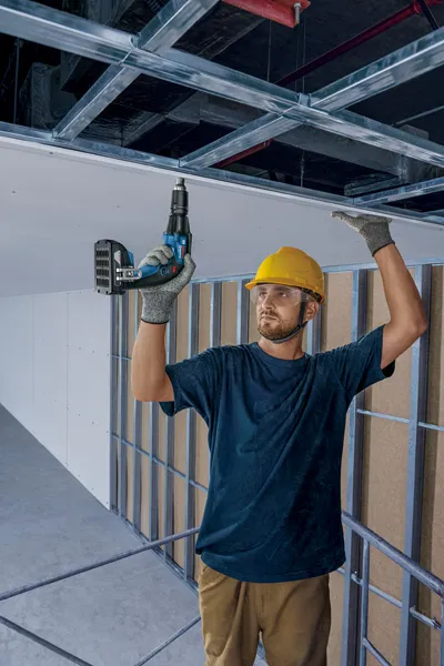 配戴安全設備的人員使用無線螺絲起子安裝乾牆。.