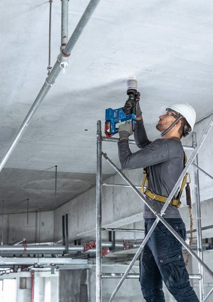 一名配戴安全設備的人站在鷹架上，用電鑽鑽天花板。.
