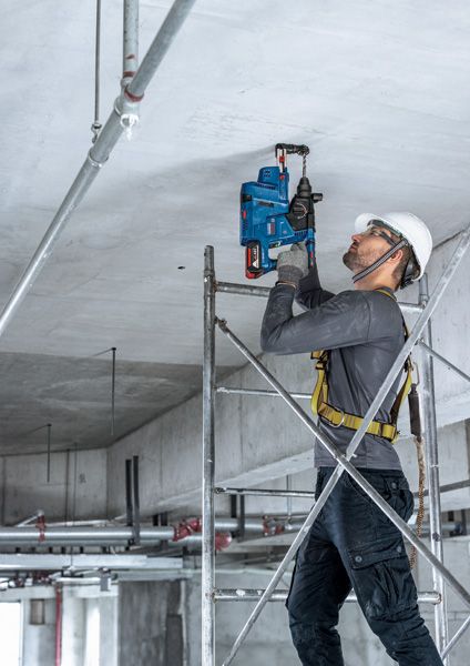 一名配戴安全設備的人員站在鷹架上，向混凝土天花板上鑽孔。.