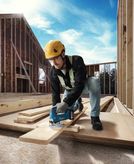 在建築工地上，一名配戴安全設備的人員正用無線曲線鋸切割木板。
