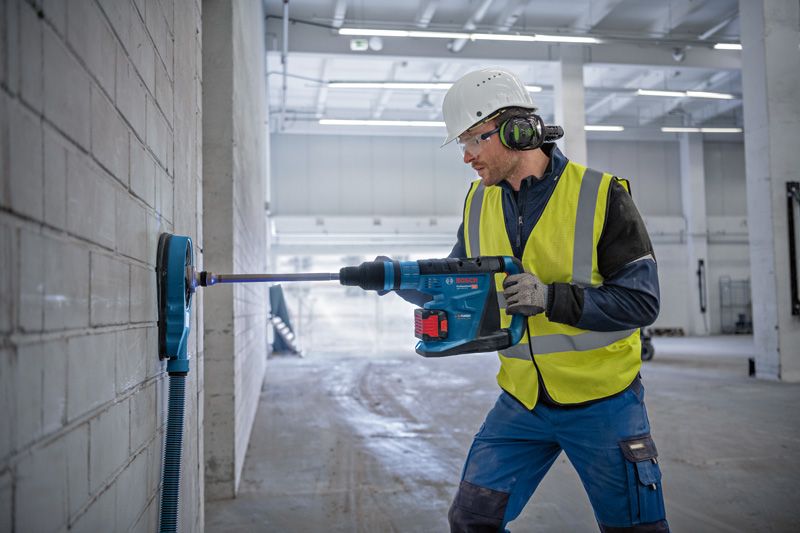 一名穿戴安全裝備的人員在大型室內空間的混凝土牆上鑽孔。