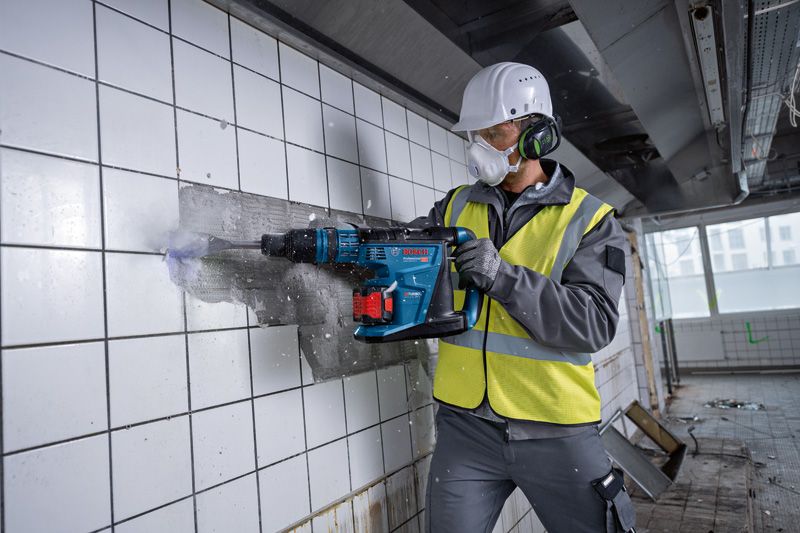 一名佩戴安全設備的人員使用無線旋轉錘從牆上拆除瓷磚。.