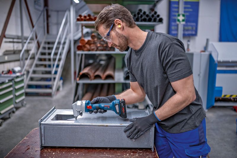 一名配戴安全設備的人員正在使用無線剪斷機修整金屬板。.