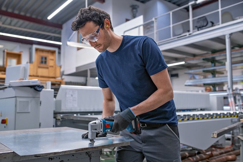 一名配戴安全設備的人員正在使用無線金屬剪剪切金屬板。.