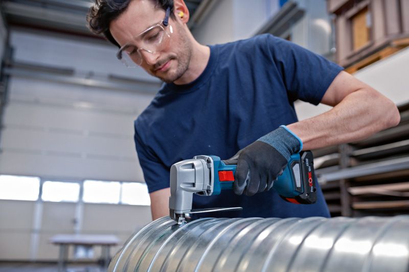 一名配戴安全設備的人員使用無線金屬剪剪斷金屬管路。.