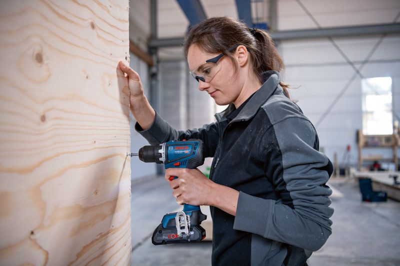 一名佩戴安全設備的工人在車間內鑽木板。.