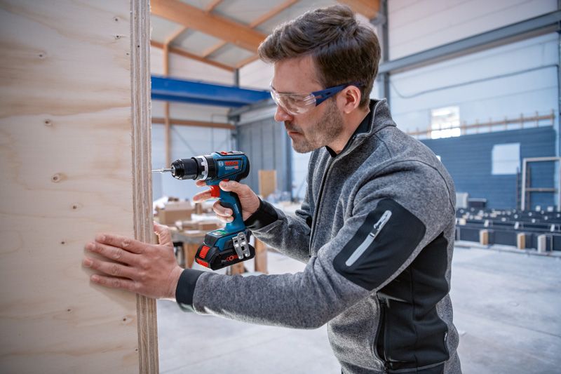 穿著安全設備的人員在車間內鑽入木板。.