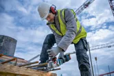 在建築工地上，一名配戴安全設備的工人正在用電動工具打磨鋼筋。
