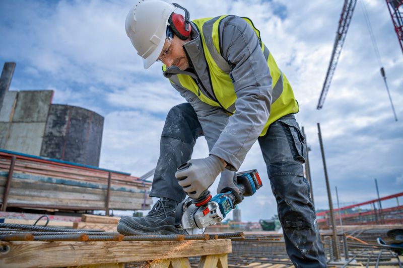 在建築工地上，一名配戴安全設備的工人正在用無線角磨機切割鋼筋。.