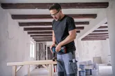 一名配戴安全設備的人員在室內建築工地上鑽木頭。