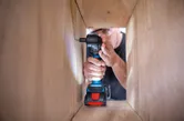 一名配戴安全設備的人員使用無線電鑽將螺絲旋入木製框架內。