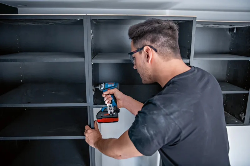 配戴安全設備的人員使用無線電鑽或起子組裝貨架。.