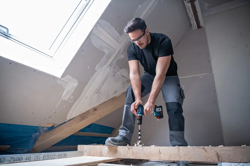 一名佩戴安全設備的人員正在一間尚未完工的閣樓內鑽木樑。.