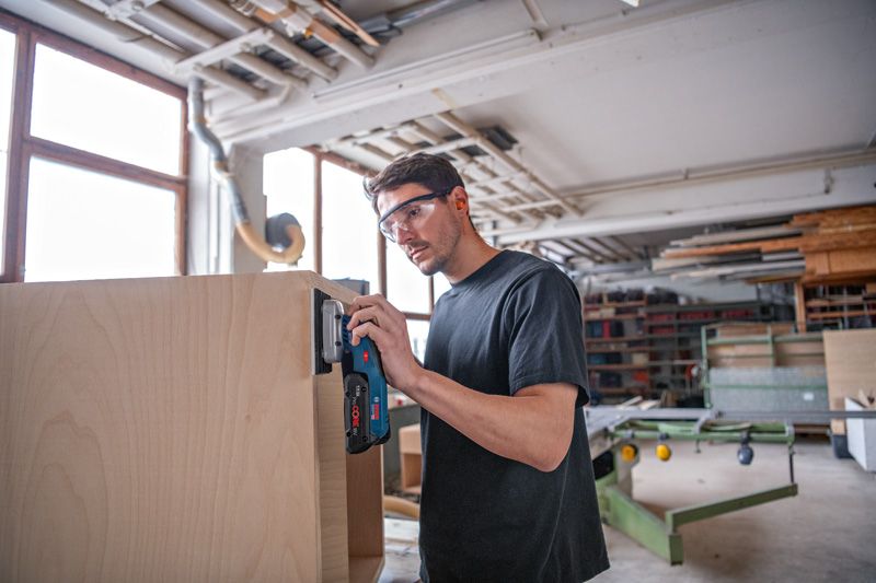 一名佩戴安全裝備的人員正在使用無線軌道砂光機打磨木製櫥櫃。.