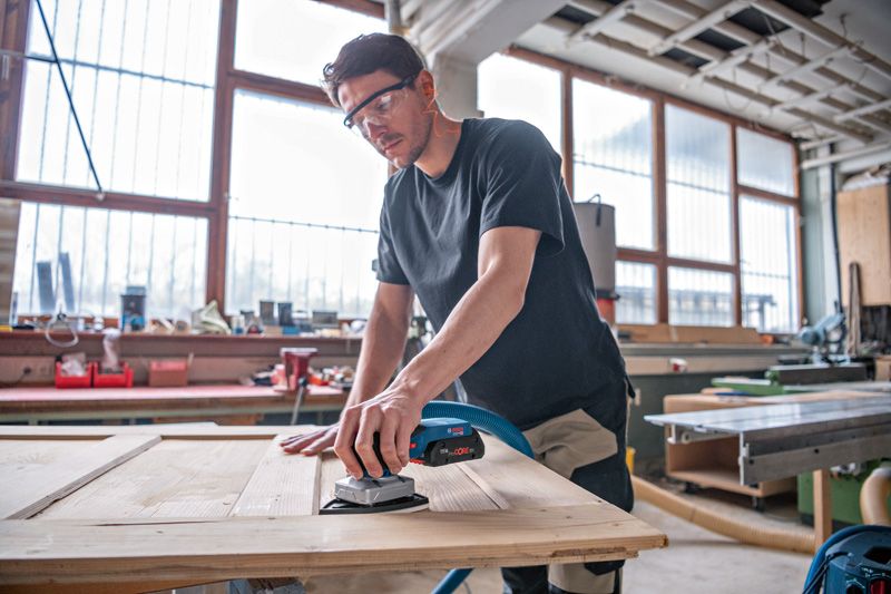 一名配戴安全裝備的人員正在使用無線軌道砂光機打磨木門。.