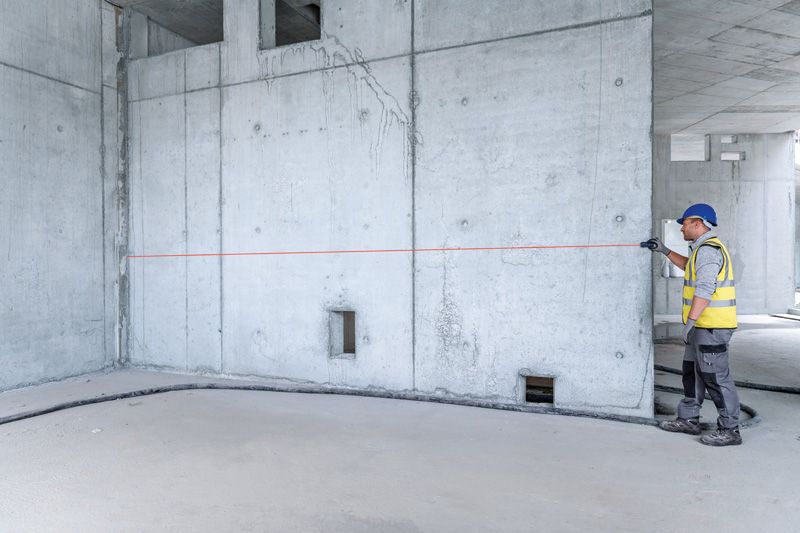 一名配戴安全設備的人員正在用雷射測量儀測量混凝土牆。.