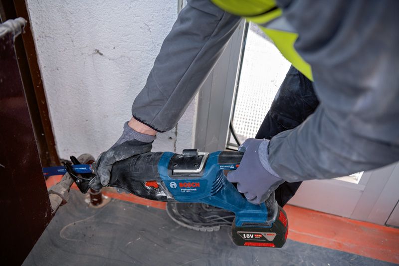 一名配戴安全設備的人員使用往復鋸切割門框附近的金屬。.