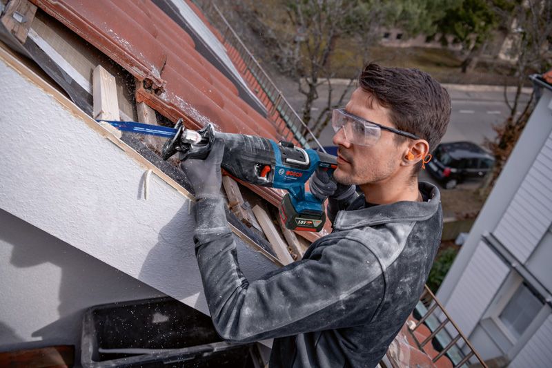 一名配戴安全設備的人員使用往復鋸在屋頂上切割木材。.