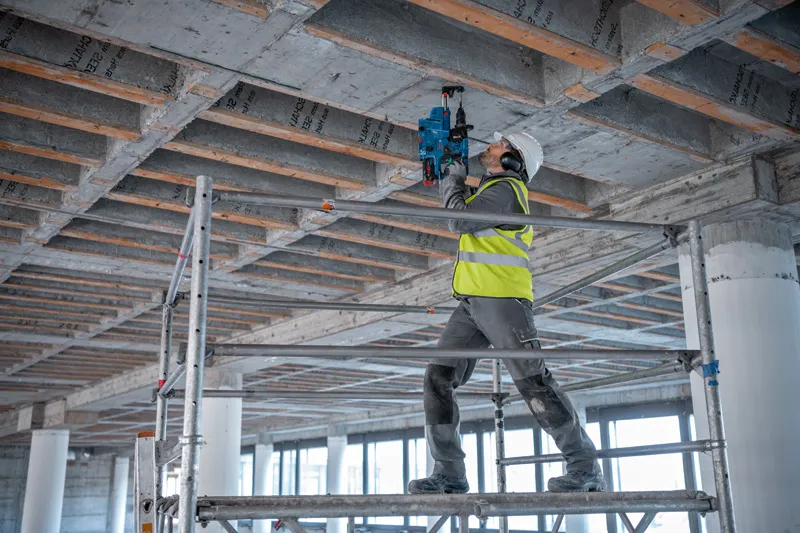 GBH 18V-28 CF 一名佩戴安全設備的人員在建築工地的混凝土天花板上鑽孔。.