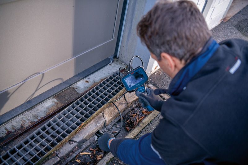 一名配戴安全設備的人員正在使用檢查攝影機檢查排水管。.