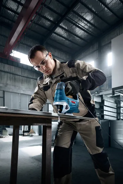 一名配戴安全設備的人員在車間使用曲線鋸切割金屬。.