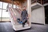 一名男子手持無線斜切鋸走下建築工地的樓梯。