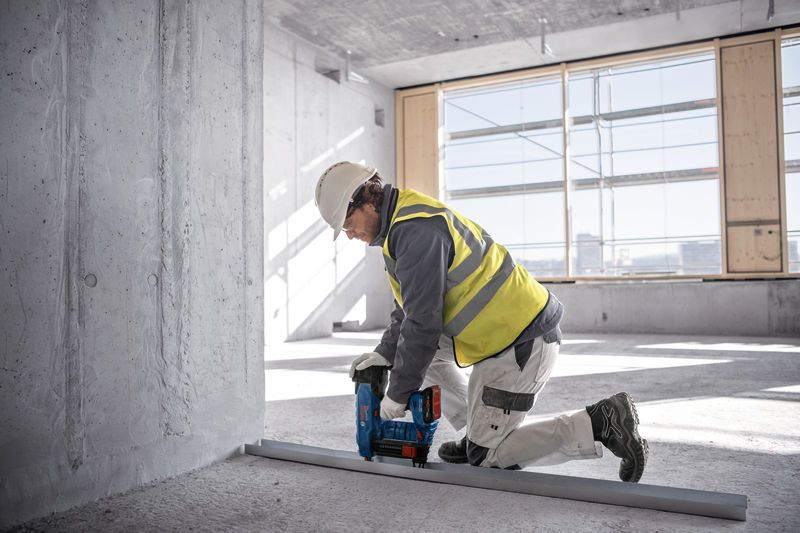 一名佩戴安全設備的人員使用無線混凝土釘槍將金屬軌道固定在地板上。.