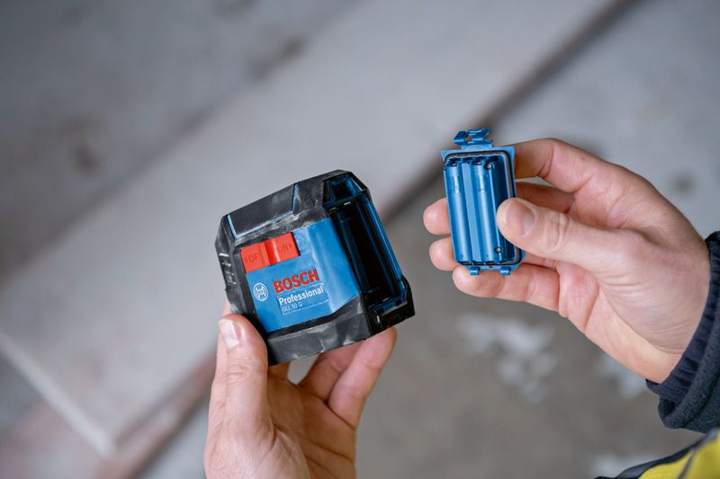 GLL 50 G 一個人在室內拿著一個藍色雷射調平工具及其電池盒。.