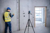 一名配戴安全設備的人員使用三腳架上的雷射調平工具在混凝土牆上做記號。