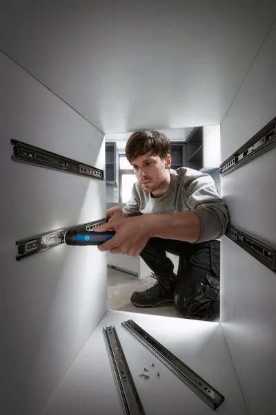 一個人使用無線螺絲起子在櫥櫃內安裝抽屜滑軌。.