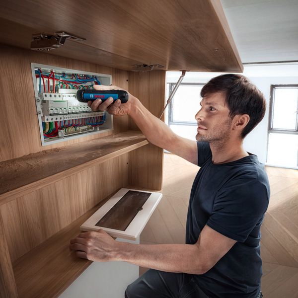 一個人使用無線螺絲起子固定配電盤中的電線。.