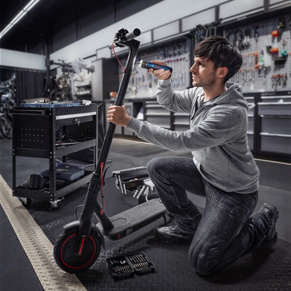 一個人跪下來，用無線螺絲起子修理電動滑板車。.