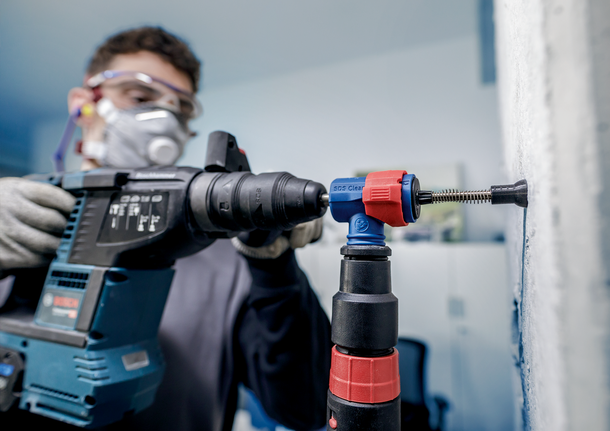 配戴安全設備的人員使用衝擊鑽在牆上鑽孔。