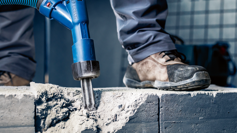 配戴安全設備的人員使用電動工具破碎混凝土。