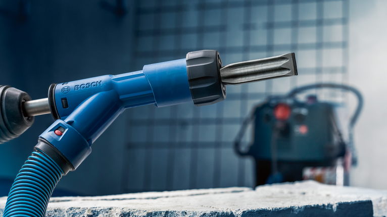 帶有鑿子附件的旋轉錘位於粗糙的混凝土塊上方。