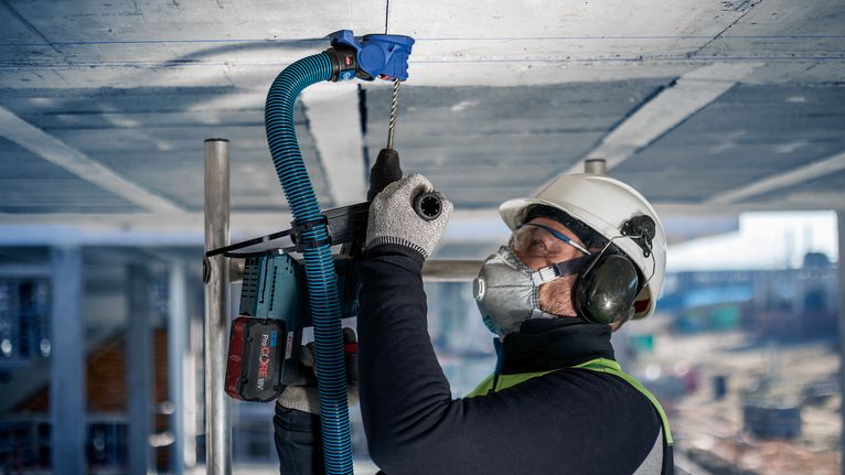 一名佩戴安全設備的人員在建築工地的混凝土天花板上鑽孔。