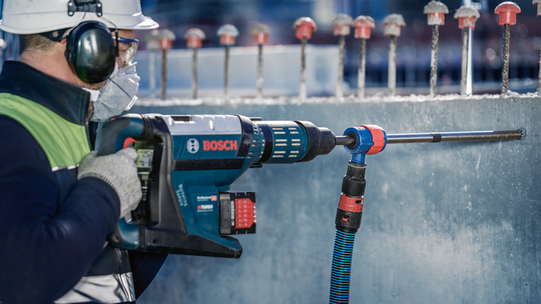 EXPERT SDS Clean max-8X 五溝鎚鑽鑽頭套裝 20 x 400 x 650 一名配戴安全設備的人員使用旋轉錘在混凝土中鑽孔。