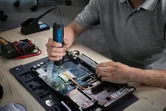 一個人在工作台上使用無線螺絲起子組裝筆記型電腦。